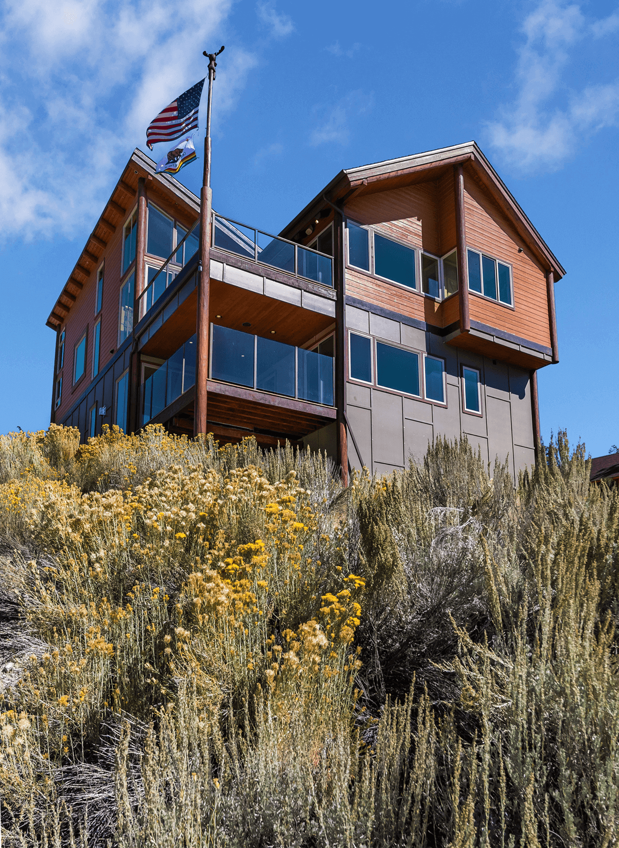 Eagle Lake Project - Sunny day view from bottom of slope up to house and decks - Dean Larkin Design