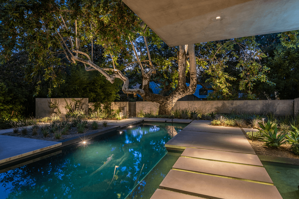 Latimer Project Pool at night with walkway to a tree at the end next to a wall | outdoor entertainment spaces in architecture design projects - Dean Larkin Design