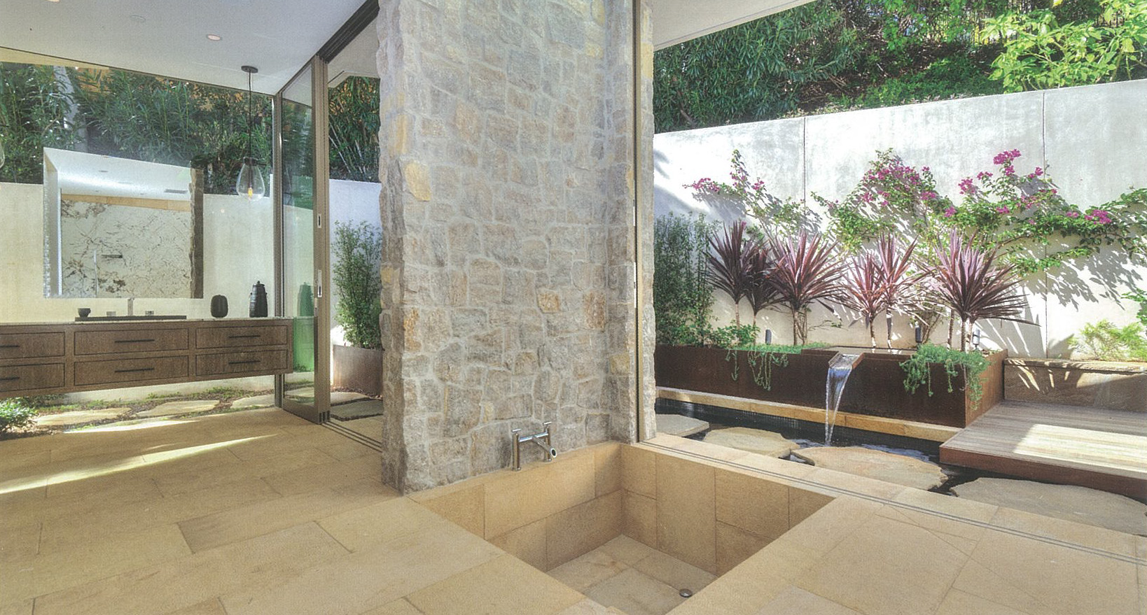 Blue Jay bathroom with sunken tub beside water feature and looking out through a glass wall into a courtyard with purple plants - Indoor/Outdoor Design - Dean Larkin Design